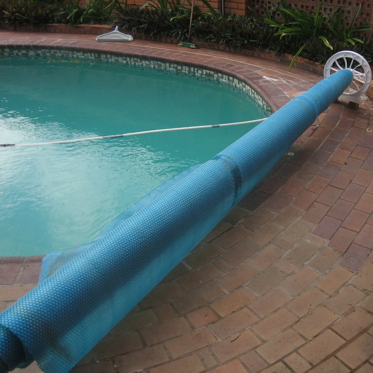 Manta térmica solar azul de burbujas enrollada en su carrete junto a una piscina