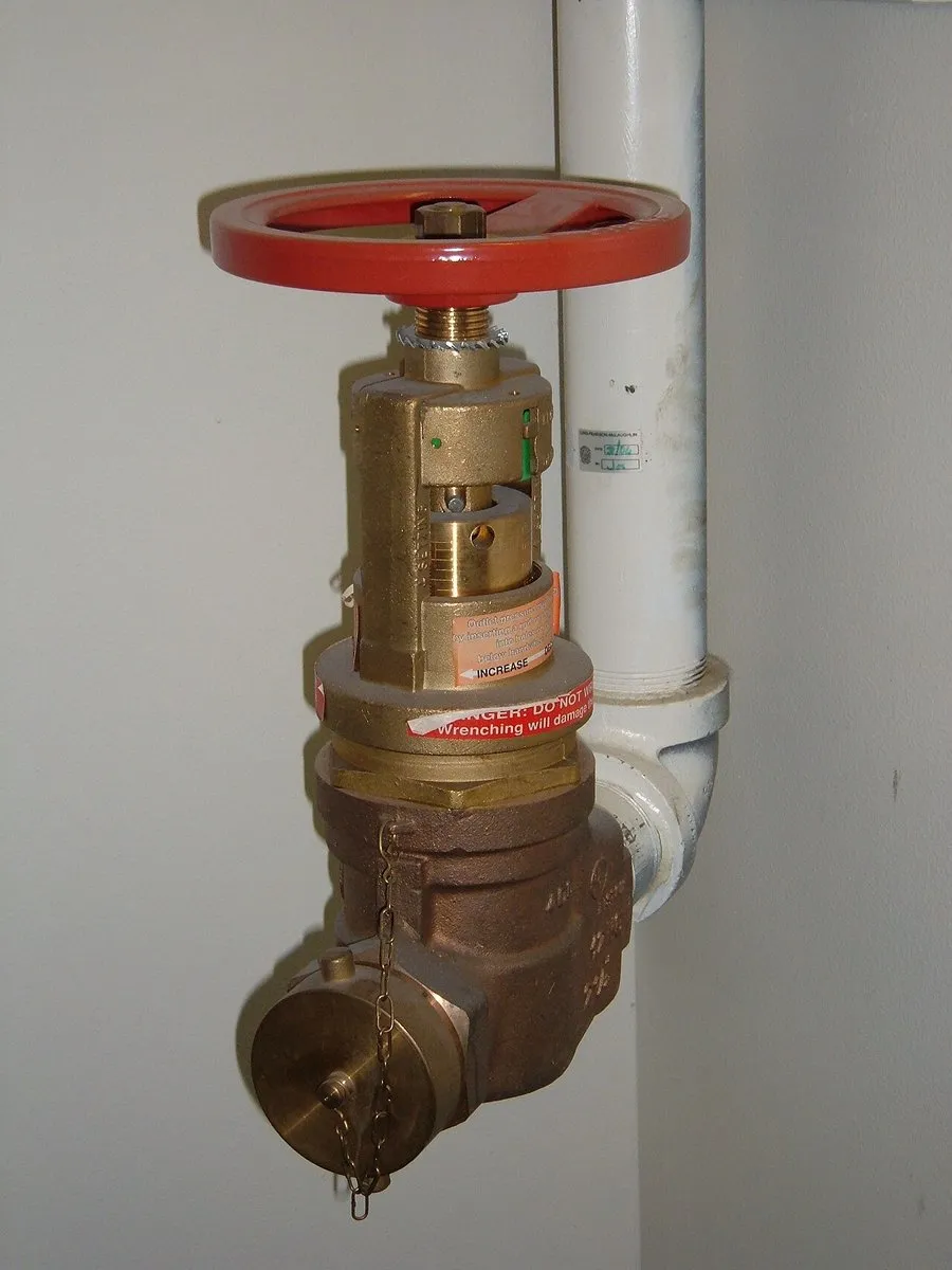 Válvula angular de bronce con volante rojo instalada en una montante contra incendio, con tapa y cadena (imagen referencial)