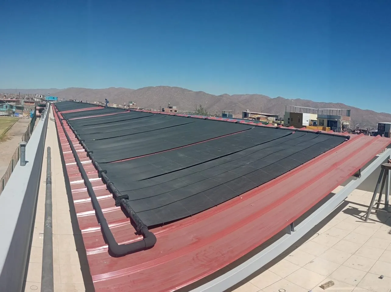 Colectores solares negros para temperado de piscina instalados sobre el techo, con los cerros de Arequipa al fondo
