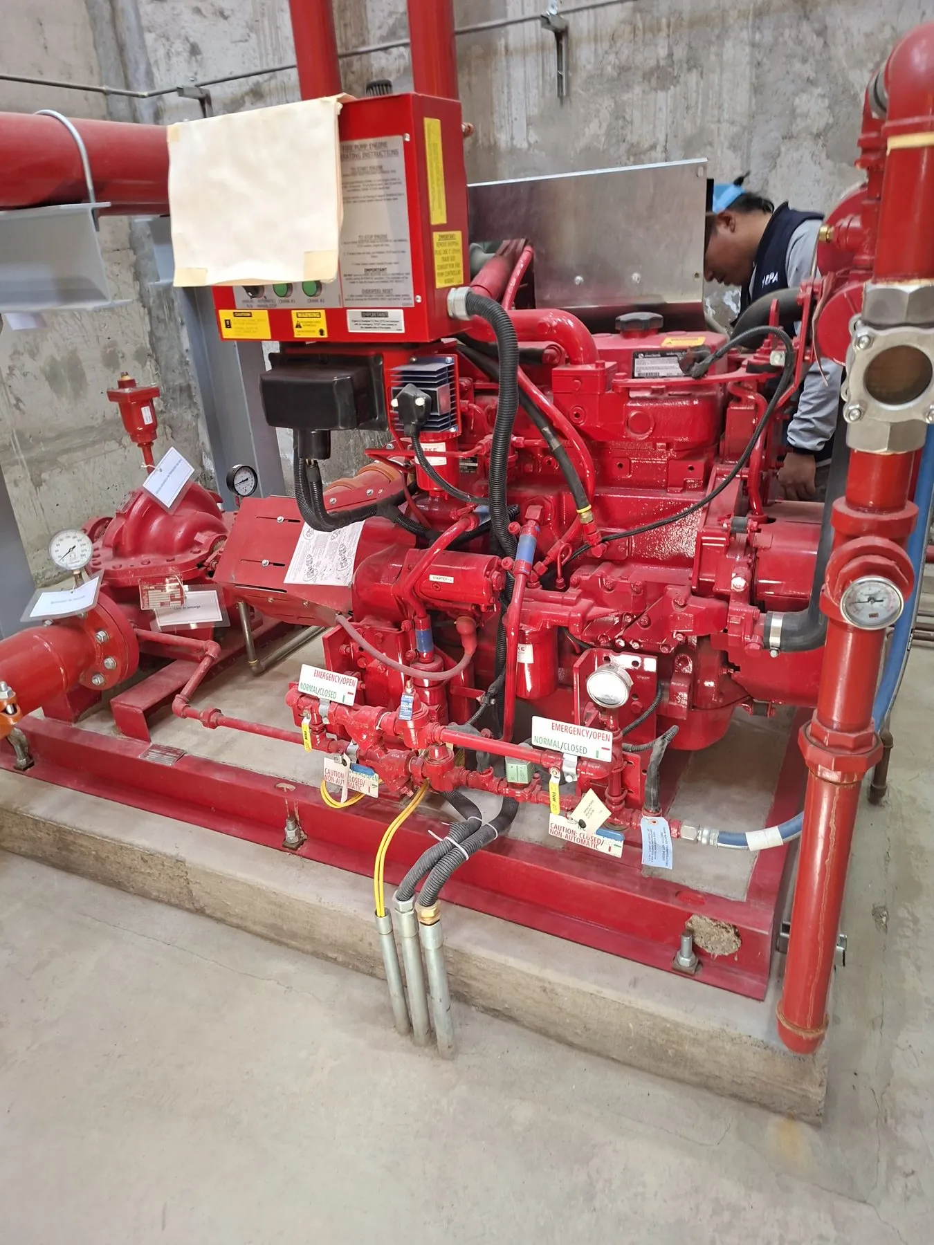 Motobomba diésel contra incendio roja sobre su base, con tablero de arranque, manómetros y tuberías de la red contra incendio